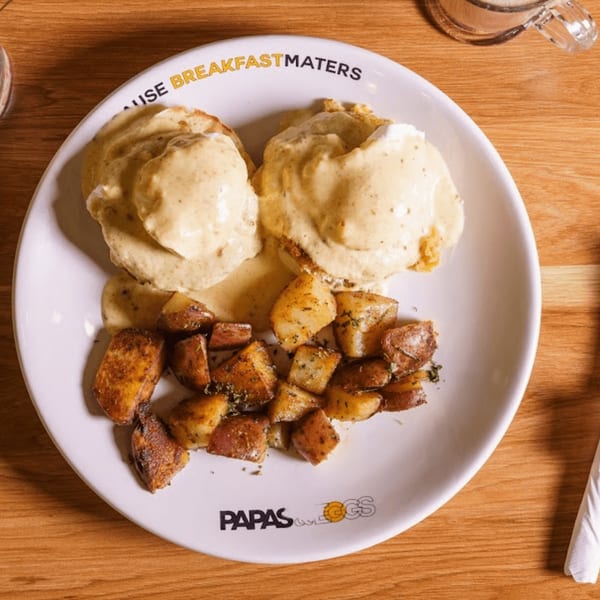 Papas and Eggs breakfast plate with eggs benedict and seasoned roasted potatoes on a wooden table.
