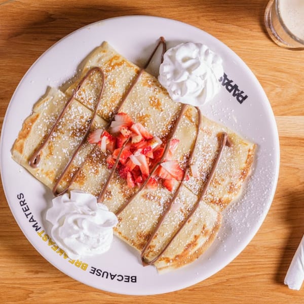 Papas and Eggs' crepes with chocolate drizzle, powdered sugar, strawberries, and whipped cream.