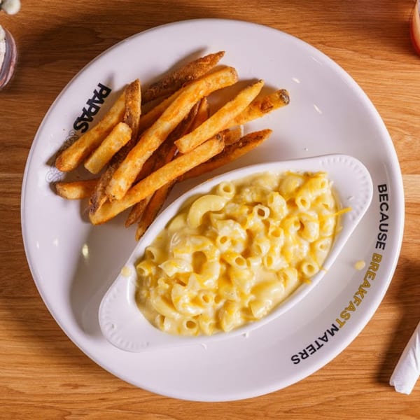 A white plate with Papas and Eggs fries and a side of creamy mac and cheese.