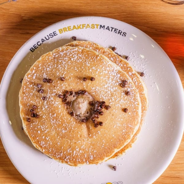 Fluffy pancakes with chocolate chips, powdered sugar, and melting butter on a white plate.