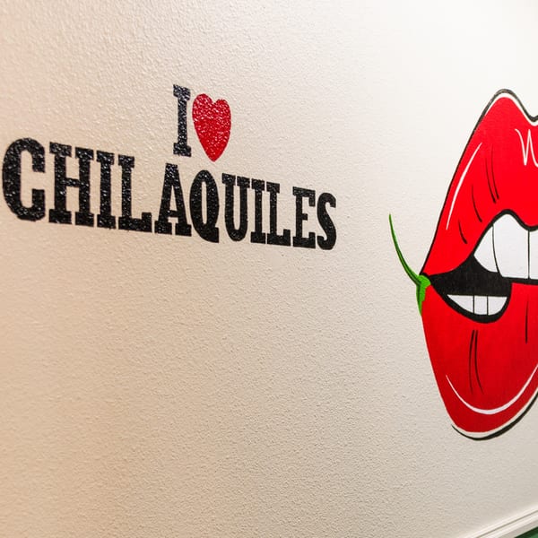 A wall mural with "I ❤️ CHILAQUILES" and a cartoon mouth biting a red chili pepper.