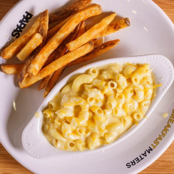 A white plate with a side of golden french fries and a bowl of creamy macaroni and cheese.