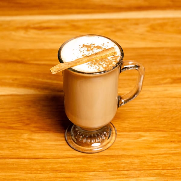 A Papas and Eggs latte with whipped cream, cinnamon powder, and a cinnamon stick.