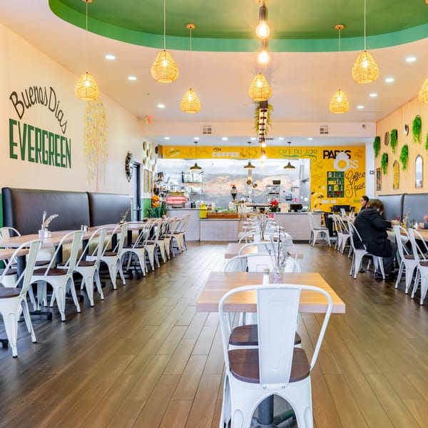 Bright, spacious interior of Papas and Eggs restaurant with white tables, black booths, and a yellow counter.
