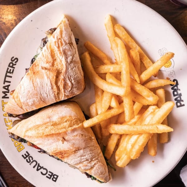 Two halves of a breakfast sandwich with dark filling and a side of golden french fries on a white plate.