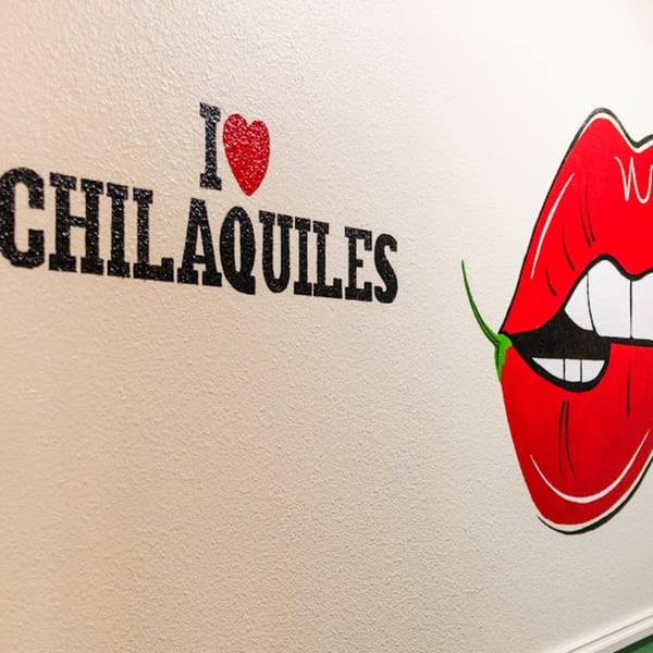 Wall art with "I ❤️ CHILAQUILES" text and red lips biting a green chili.
