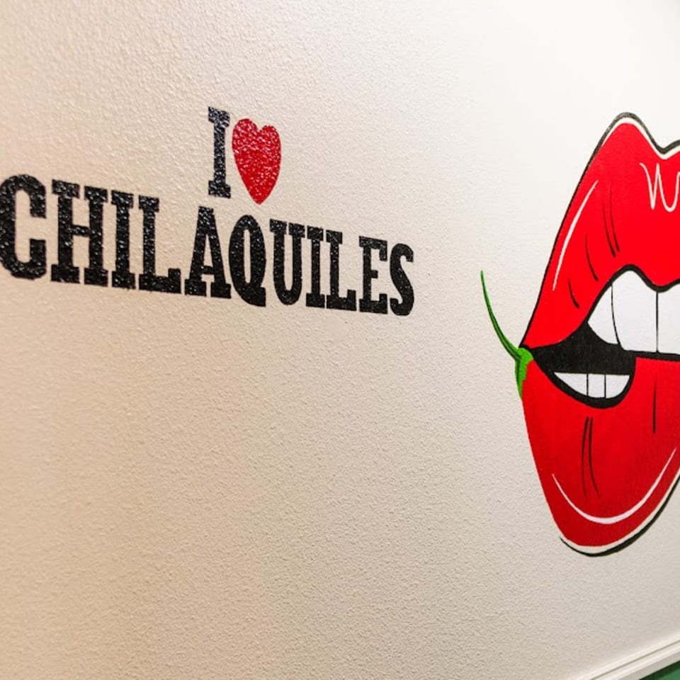 Wall art with "I ❤️ CHILAQUILES" text and red lips biting a green chili.
