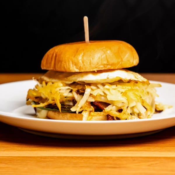 A breakfast burger with hash browns, fried egg, and a wooden skewer on a white plate.