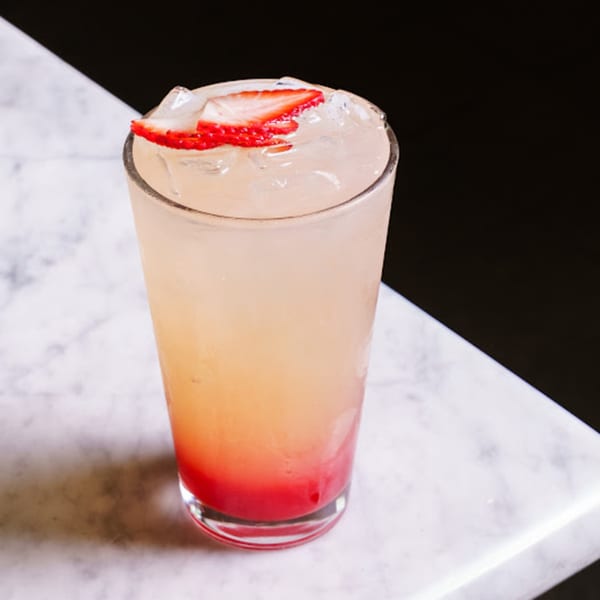Strawberry lemonade with ice and strawberry slices on a white marble surface.