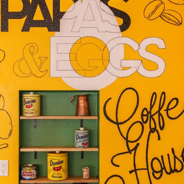 A yellow wall with "Papas & Eggs Coffee House" text and shelves holding vintage sugar and coffee cans.