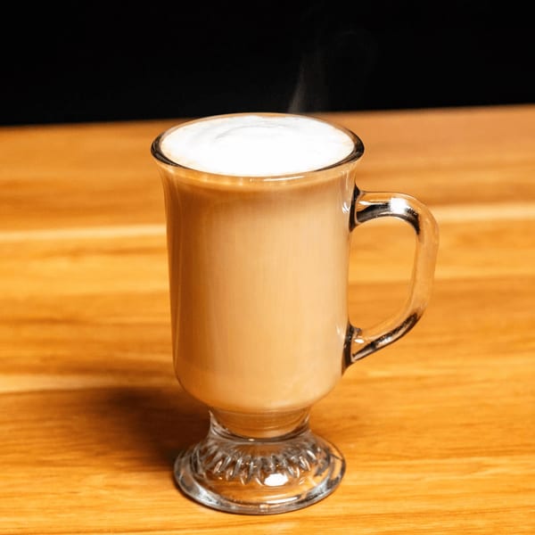 Steaming latte with foamed milk in a clear glass mug on a wooden table at Papas and Eggs.