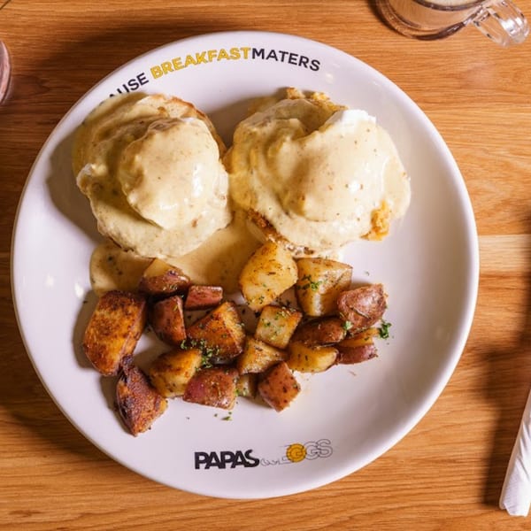 Two eggs benedict with hollandaise sauce and a side of seasoned breakfast potatoes on a white plate.