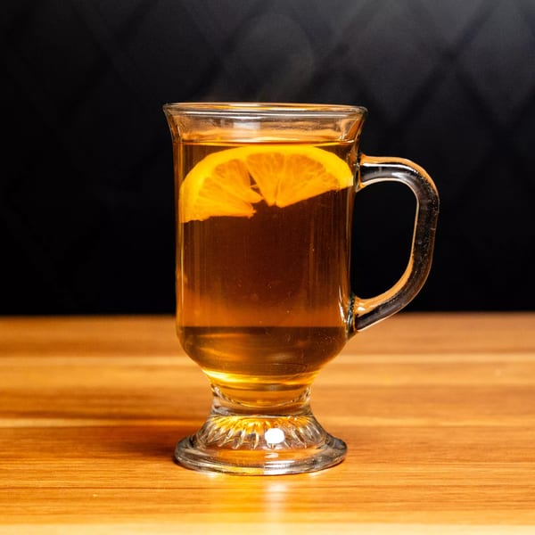 Steaming hot tea with a lemon slice in a clear mug on a wooden table.