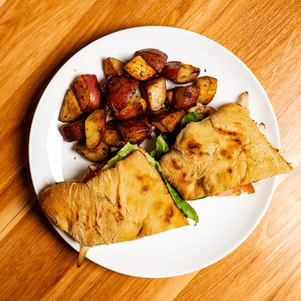 Papas and Eggs' breakfast plate with a panini sandwich and roasted red potatoes on a white plate.