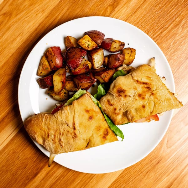 A Papas and Eggs breakfast plate with a sandwich and roasted potatoes on a white plate.