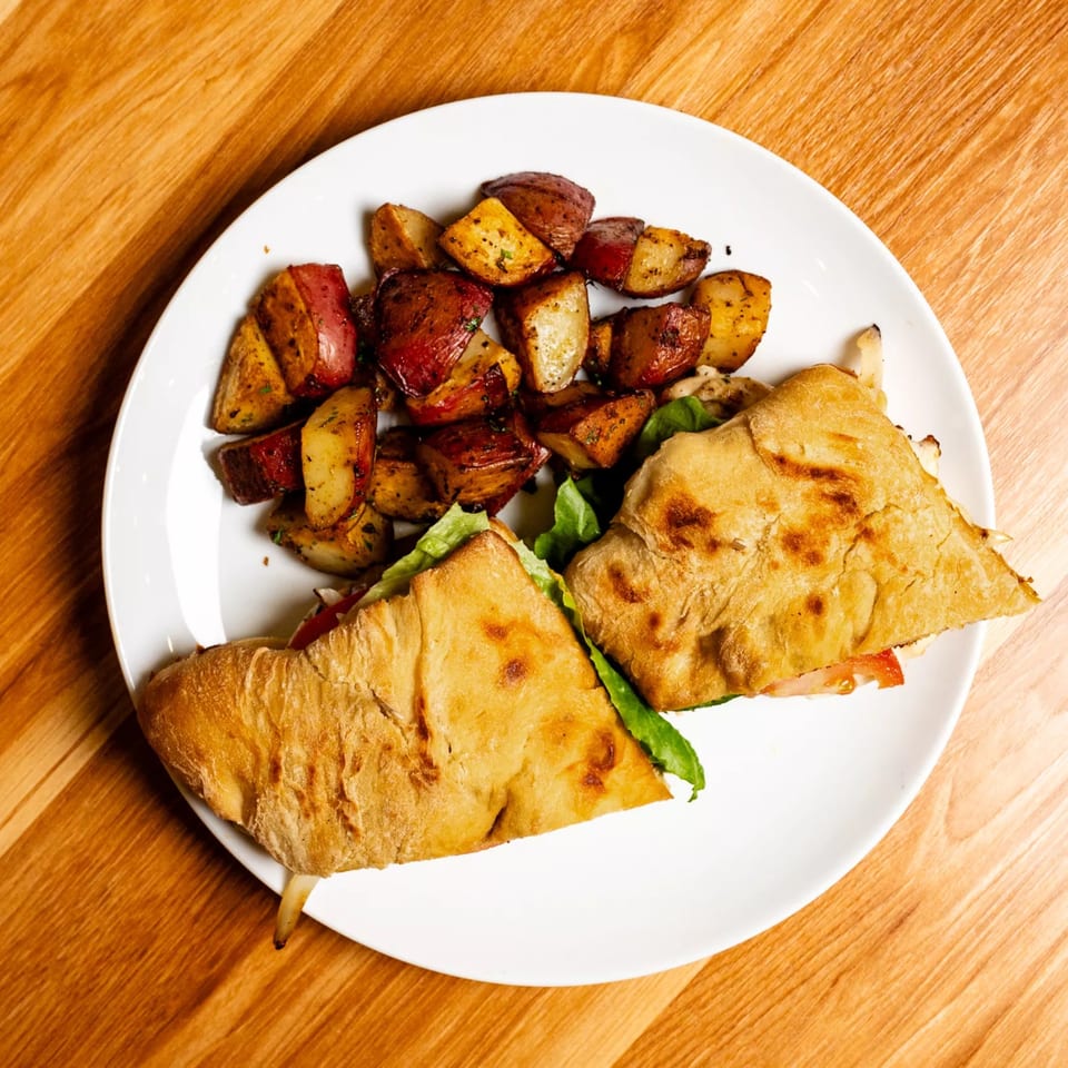 A Papas and Eggs breakfast plate with a sandwich and roasted potatoes on a white plate.