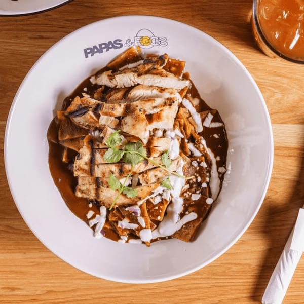 Papas and Eggs' chilaquiles with grilled chicken, mole sauce, cheese, and cilantro on a white plate.